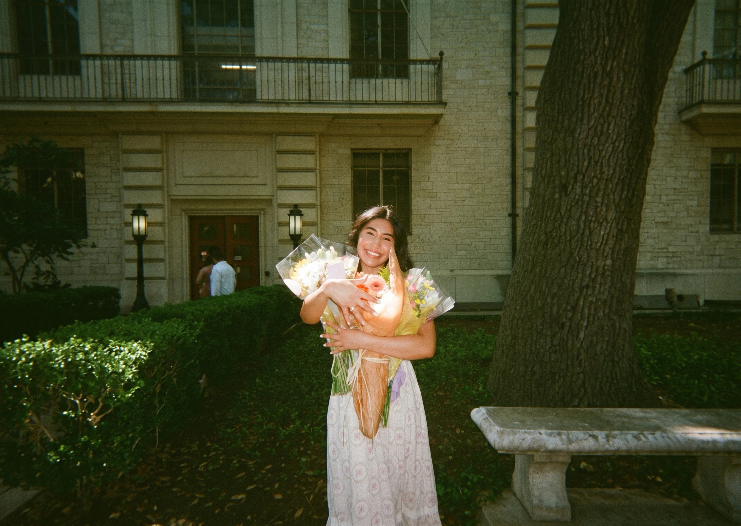 Hewitt graduate holding bouquets outside the school