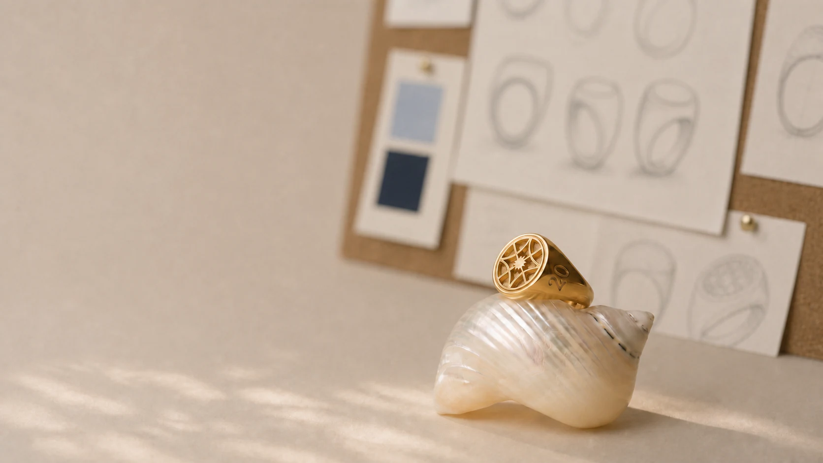Gold Hewitt class ring displayed on a shell with softly blurred ring studies behind it