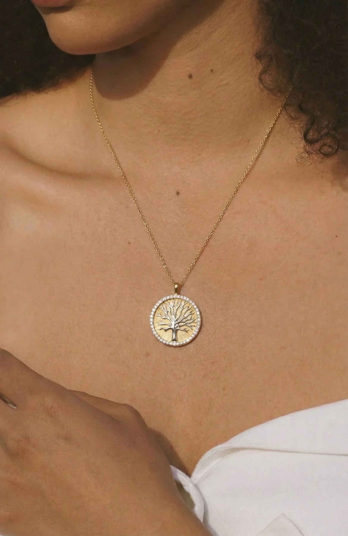 Gold tree medallion necklace worn against a white top